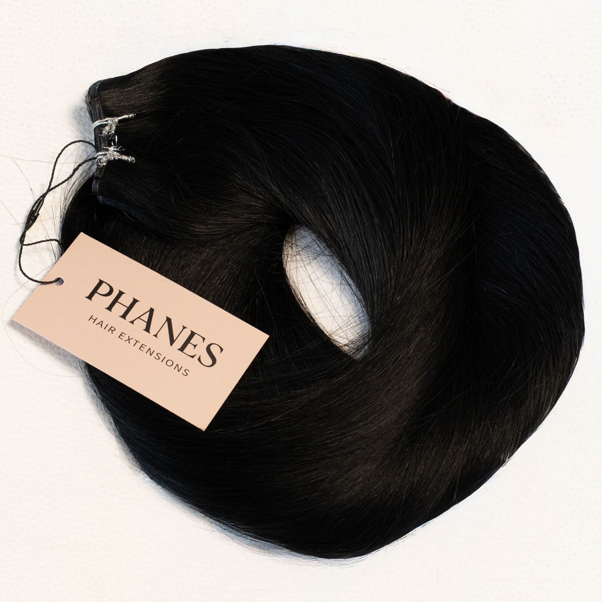 A bundle of black hair extensions with a beige paper tag reading PHANES, photographed on a clean white background. (Jet Black / #1)