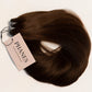 A bundle of dark brown hair extensions with a pink paper tag reading PHANTASY Hair Extensions, laid flat on a light off-white background. (Dark Brown / #2)