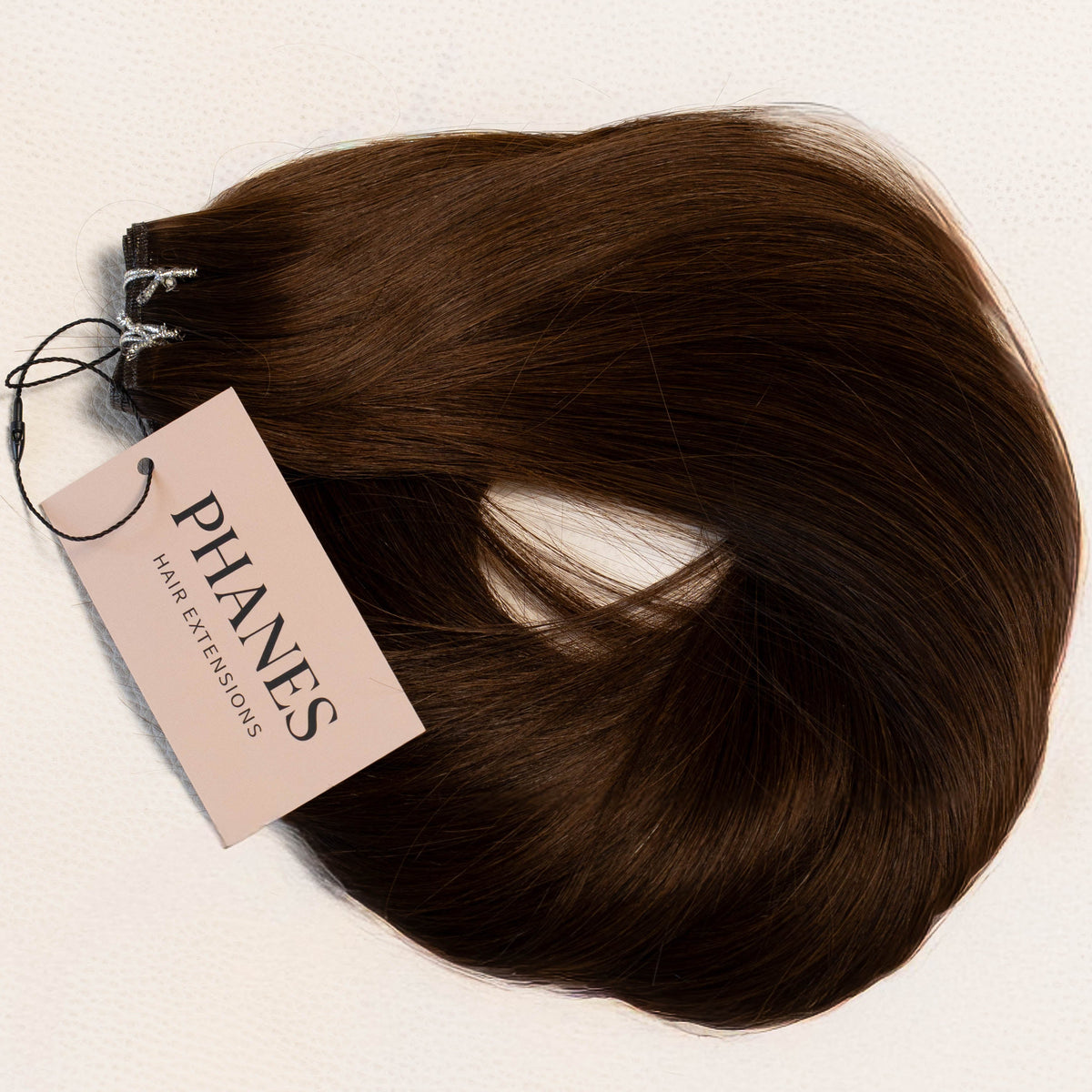 A bundle of dark brown hair extensions with a pink paper tag reading PHANTASY Hair Extensions, laid flat on a light off-white background. (Dark Brown / #2)
