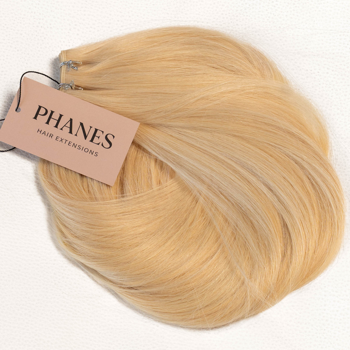 A bundle of blonde hair extensions with a pink tag reading PHANES HAIR EXTENSIONS, laid on a white background. (Warm Blonde / #22)