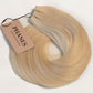 A bundle of blonde hair extensions with a light brown paper tag reading PHANES, arranged in a loose coil on a white textured background. (Ice Blondest / #24A)