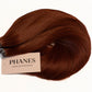 A bundle of PHANES hair extensions in a warm auburn brown color, with a beige paper label attached, set against a plain white background. (Fire Red / #34)