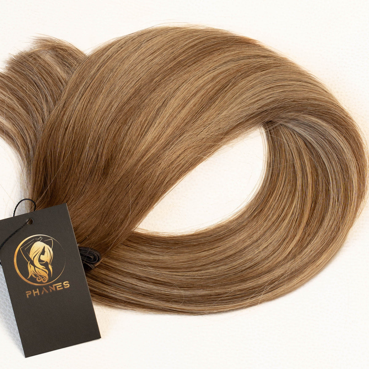 A bundle of straight, light brown hair extensions with subtle warm blonde highlights, displayed on a clean white background with a black brand tag attached. (California Blonde / B4/24)