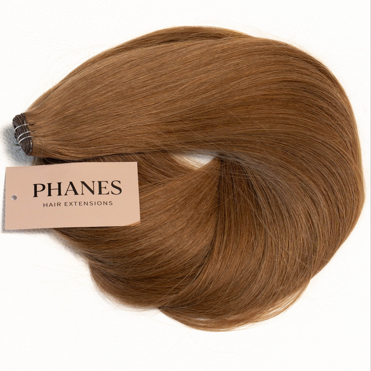 A bundle of PHANES clip-in hair extensions in a warm medium brown shade, with a beige paper label attached, set against a plain white background. (Light Brown / #6)