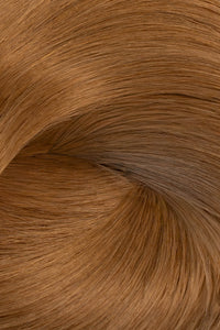 A close-up texture shot of a hair color swatch, showing fine strands of light brown hair with warm golden and caramel undertones arranged in a soft swirl. (Caramel / #8)