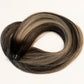 A looped section of synthetic or human hair extensions with a dark brown to black base and warm blonde highlights, arranged in a circle on a plain white background. (Jersey Balayage B1b/60)