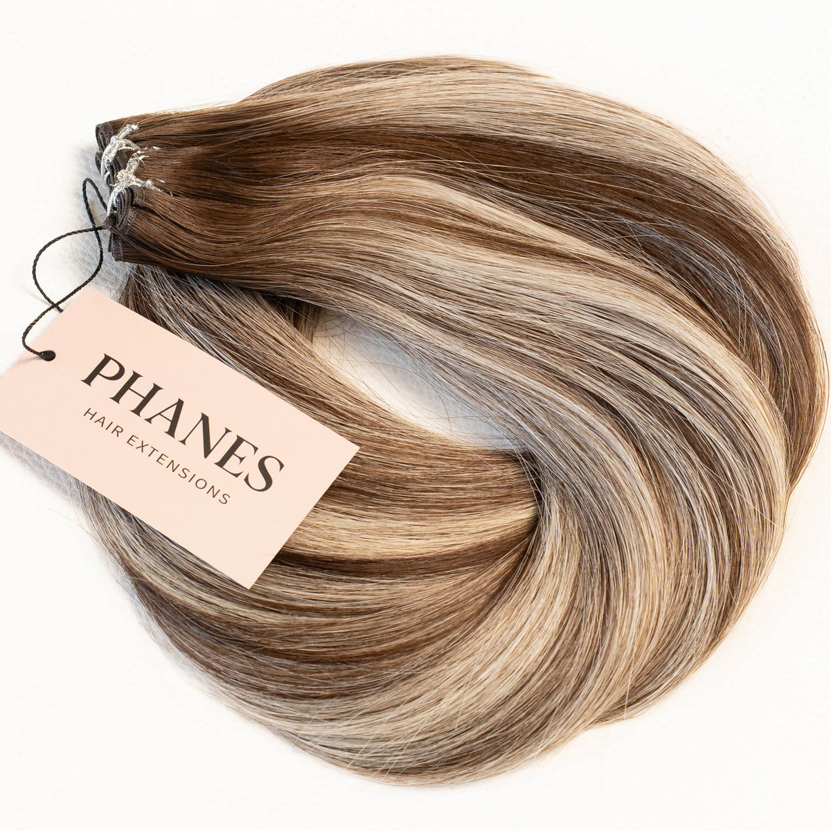 A bundle of Phanes hair extensions in a light brown and blonde ombré color, with a tan Phanes Hair Extensions tag attached, set against a plain white background. (Boston Balayage B2/60)