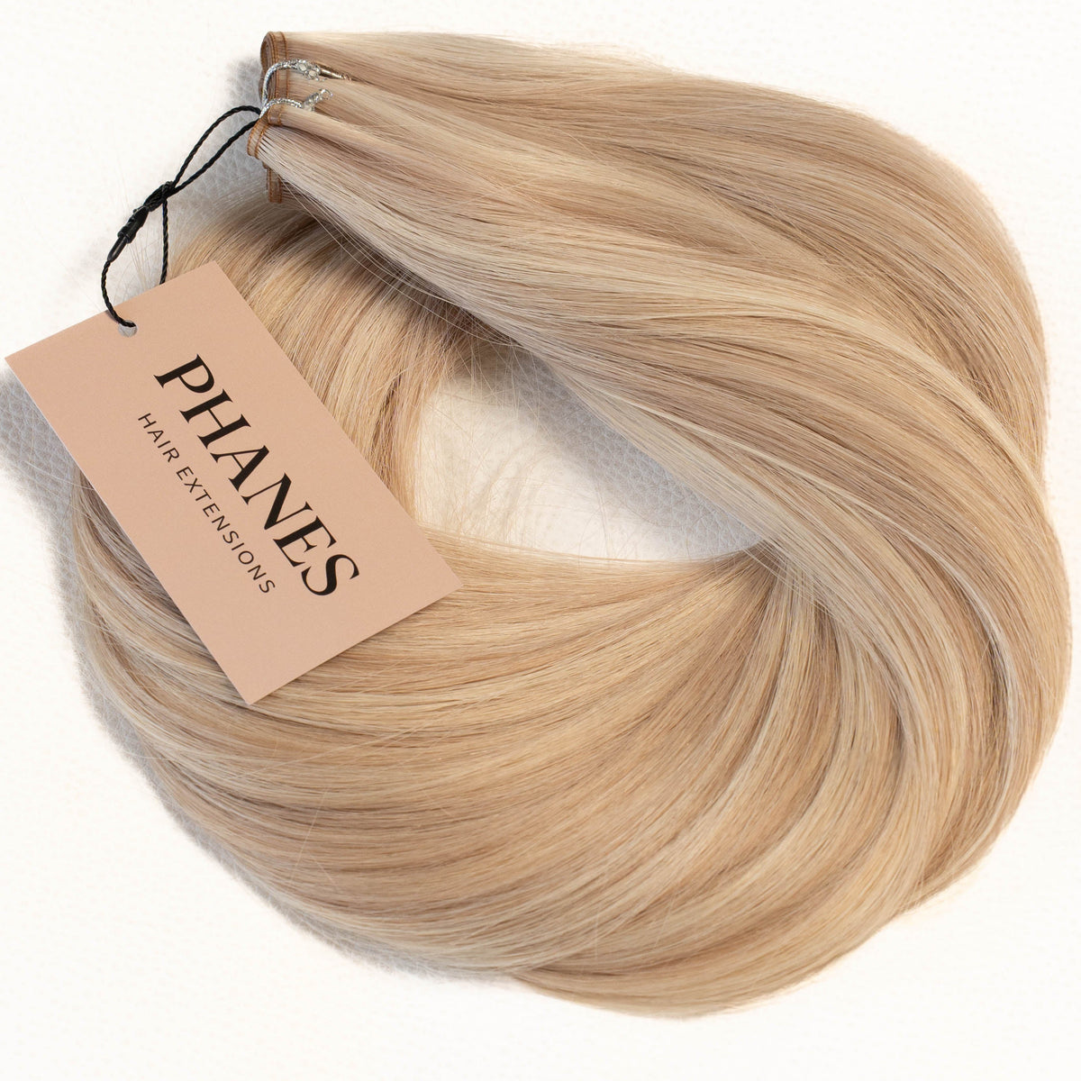 A bundle of blonde hair extensions with a beige paper tag reading PHANES, displayed on a clean white background. (Pearl Piano / FB)