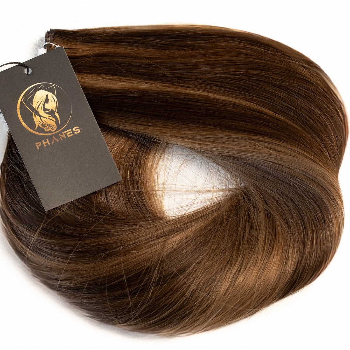 A bundle of medium brown hair extensions with a dark gray tag featuring a gold logo, set against a plain white background. (Toffee Bronde / #P2/6)