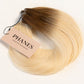 A bundle of PHANES hair extensions with a brown to blonde ombré color, featuring a light pink paper tag attached, set against a plain white background. (Rooted Blonde / #T4/60)