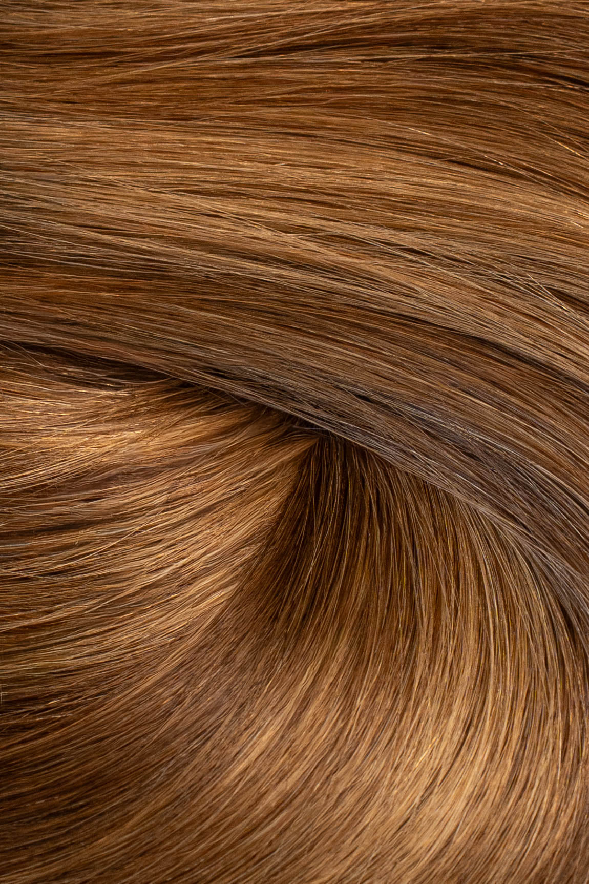 A close-up texture shot of smooth, straight brown hair with warm golden and caramel highlights, arranged in a soft swirl. (Carmel Mocha / TBF)