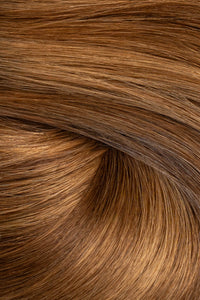 A close-up texture shot of smooth, straight brown hair with warm golden and caramel highlights, arranged in a soft swirl. (Carmel Mocha / TBF)