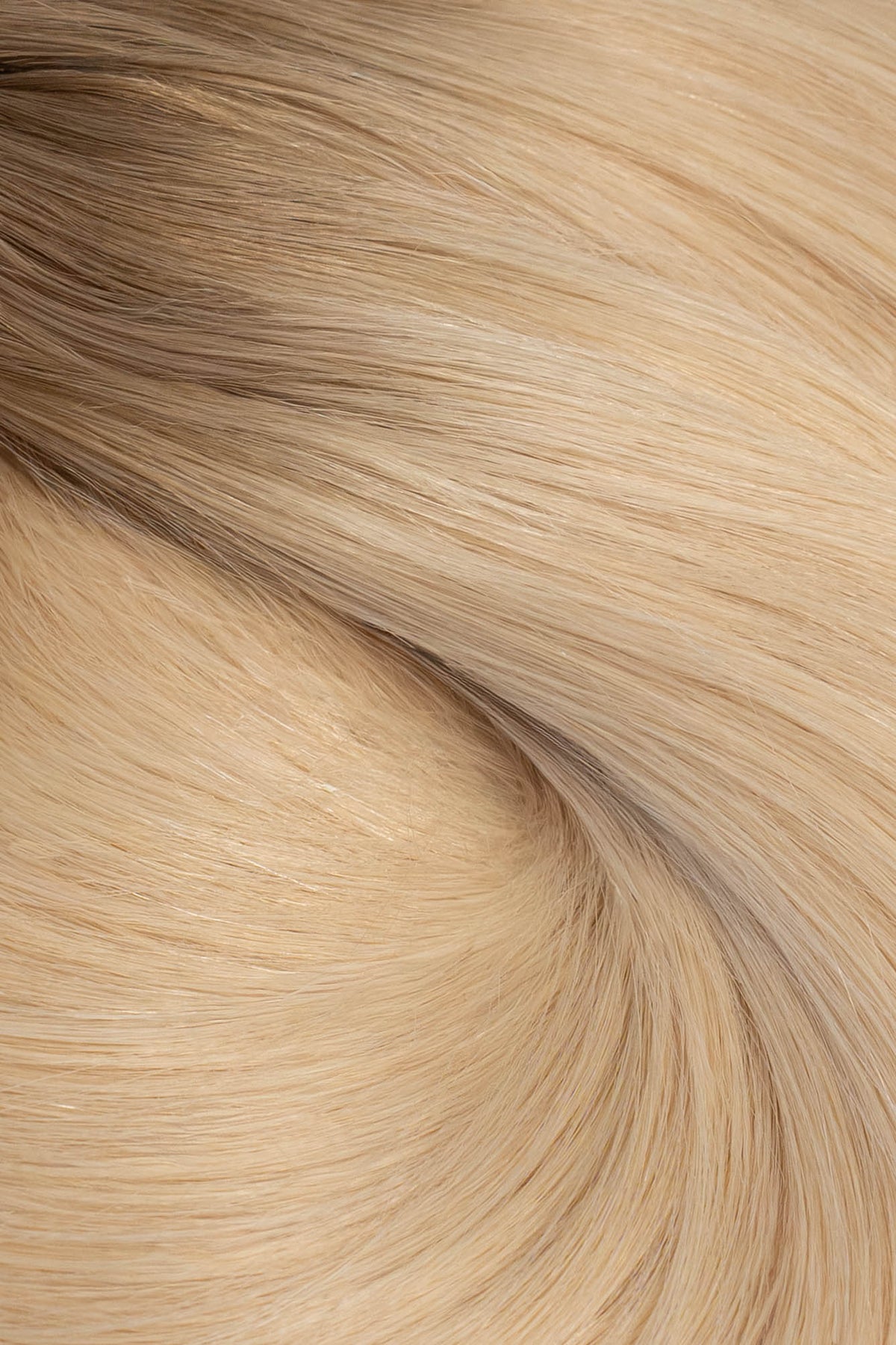 A close-up texture shot of light blonde hair with subtle warm brown lowlights, showing the fine strands and smooth flow of the hair. (Cool Ombré / #TTA)