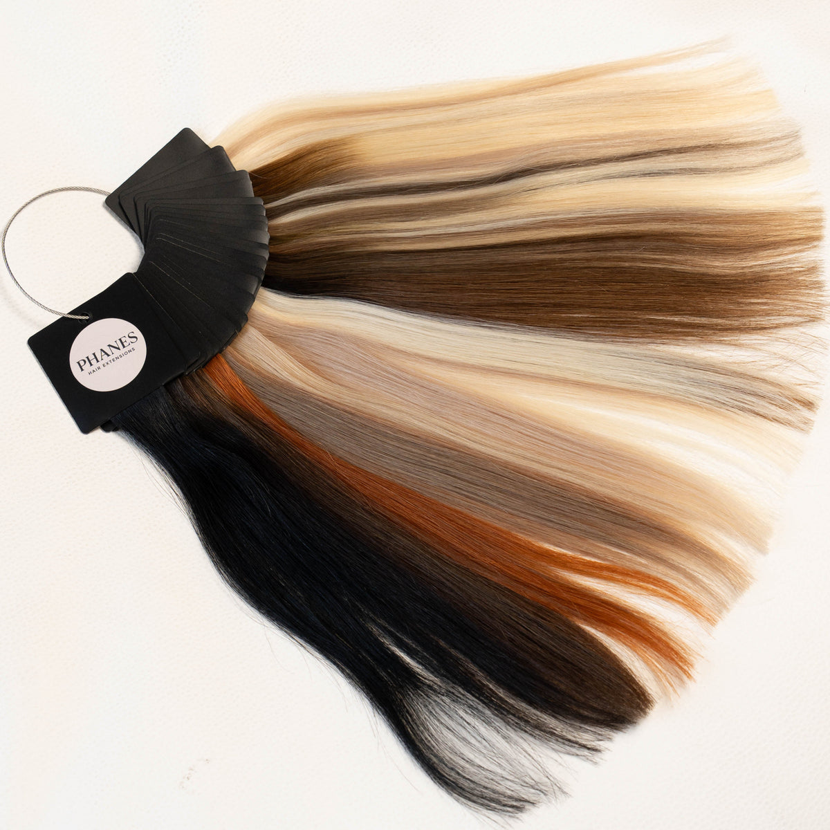 A hair color swatch fan showing multiple blended hair colors including black, brown, blonde, and copper tones, attached to a black ring holder with a visible 'MMS' label, on a plain white background.